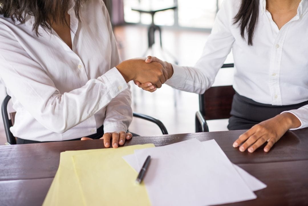 Duas mulheres apertando as mãos sobre a mesa de um escritório